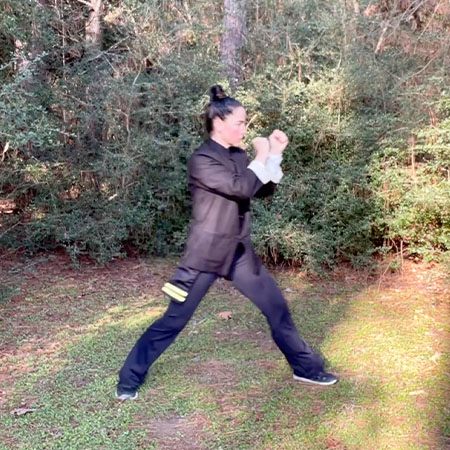 Female in forest looking to left, grabbibg hands for kung fu Training