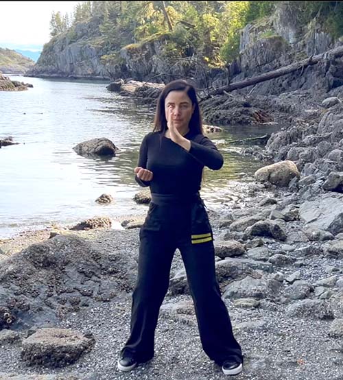 Woman on a rocky beach demonstrating wing chun wu sao with her left hand